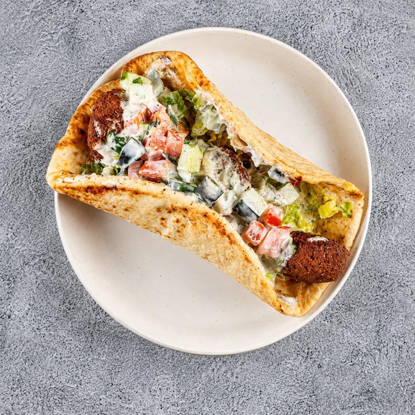 A falafel wrap filled with crispy falafel, diced tomatoes, cucumbers, and creamy white sauce.
