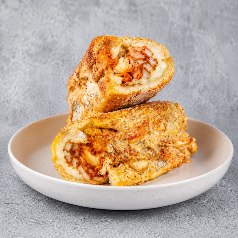 Two halves of a chicken cheesesteak sandwich, filled with melted cheese and chicken, on a white plate.