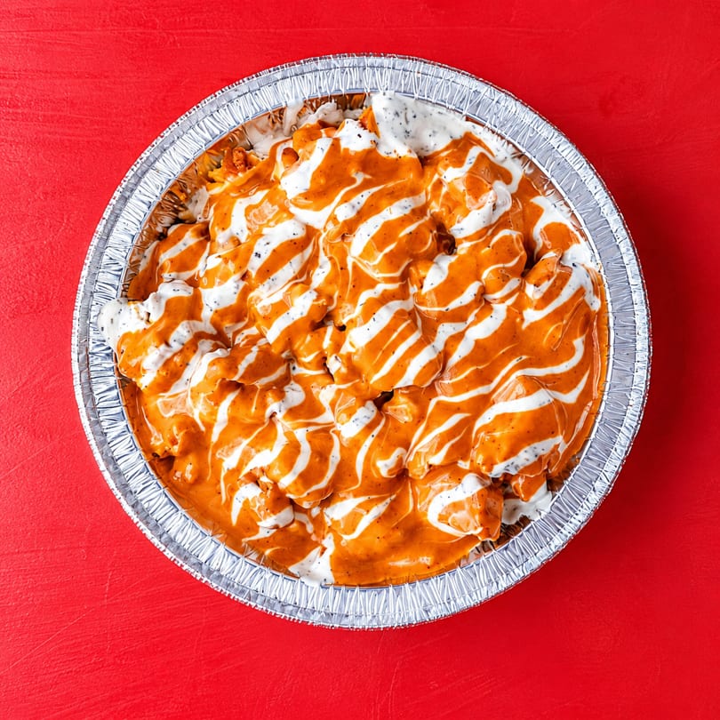 Overhead view of a foil pan filled with orange chicken and white sauce drizzled on top.