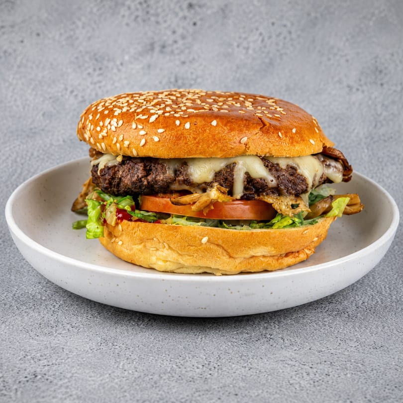 Gourmet burger with melted cheese, lettuce, tomato, and caramelized onions on a sesame bun.